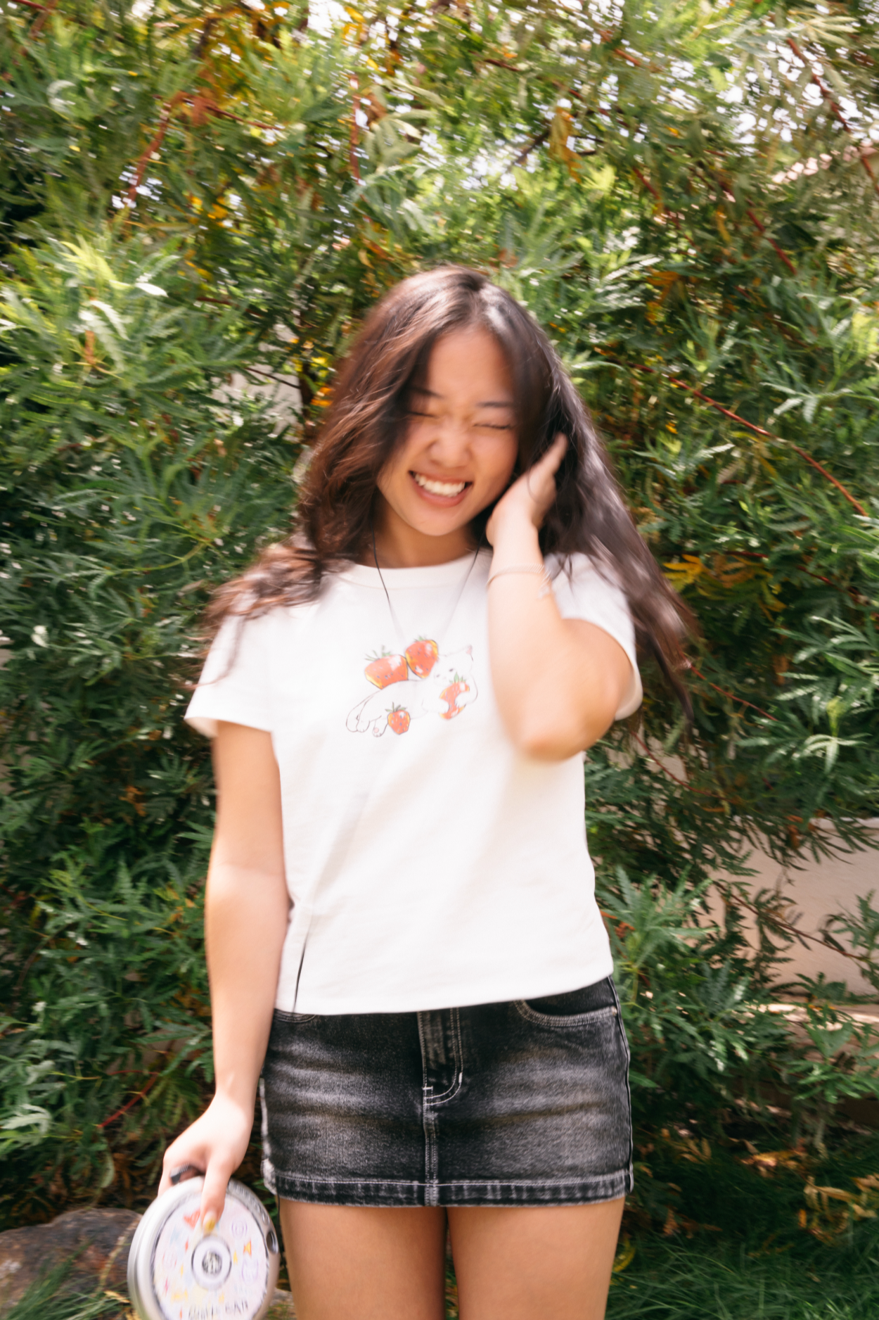 Woman wearing a white t-shirt with floral design and black denim skirt outdoors.