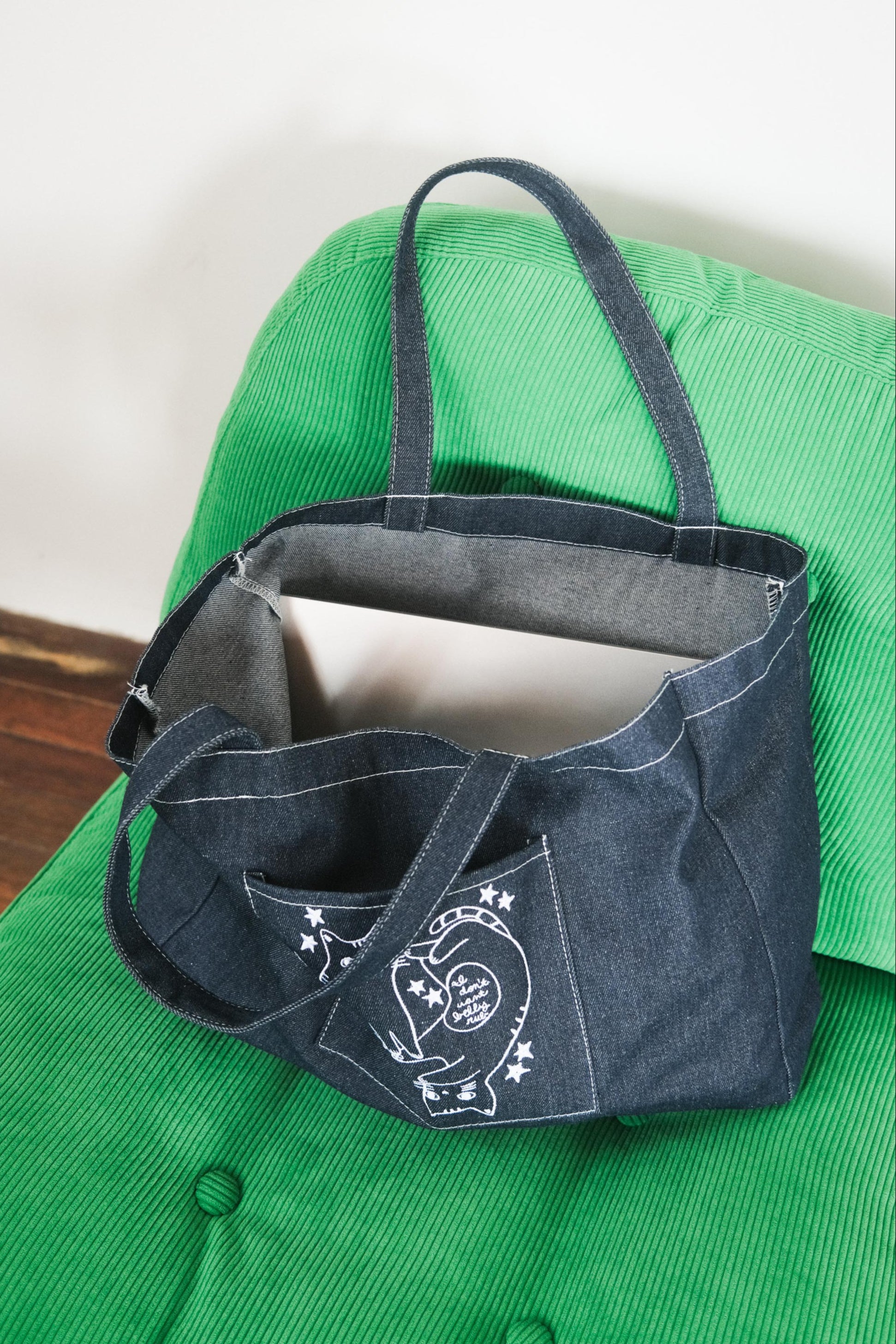 Denim tote bag with embroidered design on a green surface